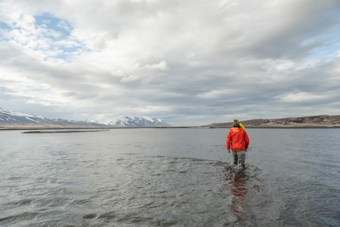 A man walking through knee deep water in a lake in Iceland.